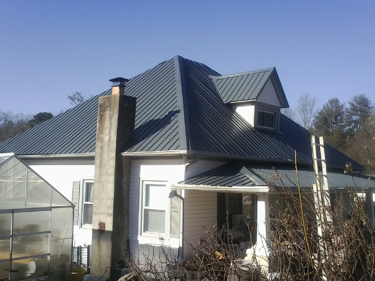 Dark blue standing seam metal roof on a white farmhouse with dormer — Slate & Tile Roof Repair by Roofing Brothers in Williston
