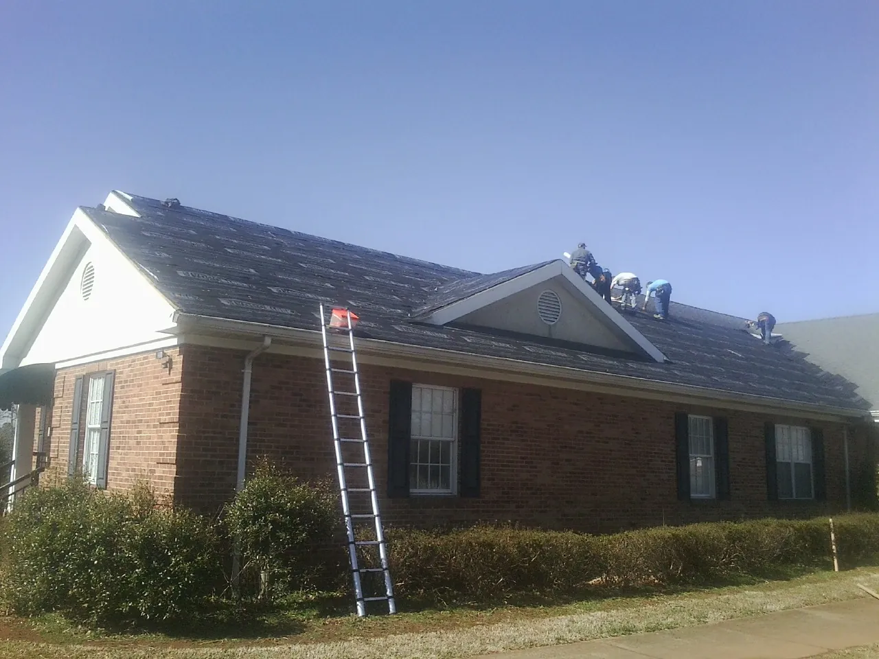 Crew tearing shingles off a brick ranch roof with a ladder set — Metal Roof Repair work by our crew in Williston