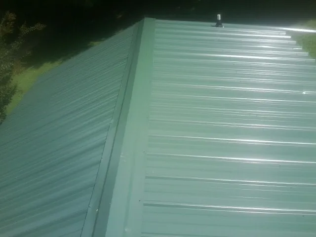 New green metal panels meeting at the ridge of a roof — Flat Roof Repair work by our crew in Williston