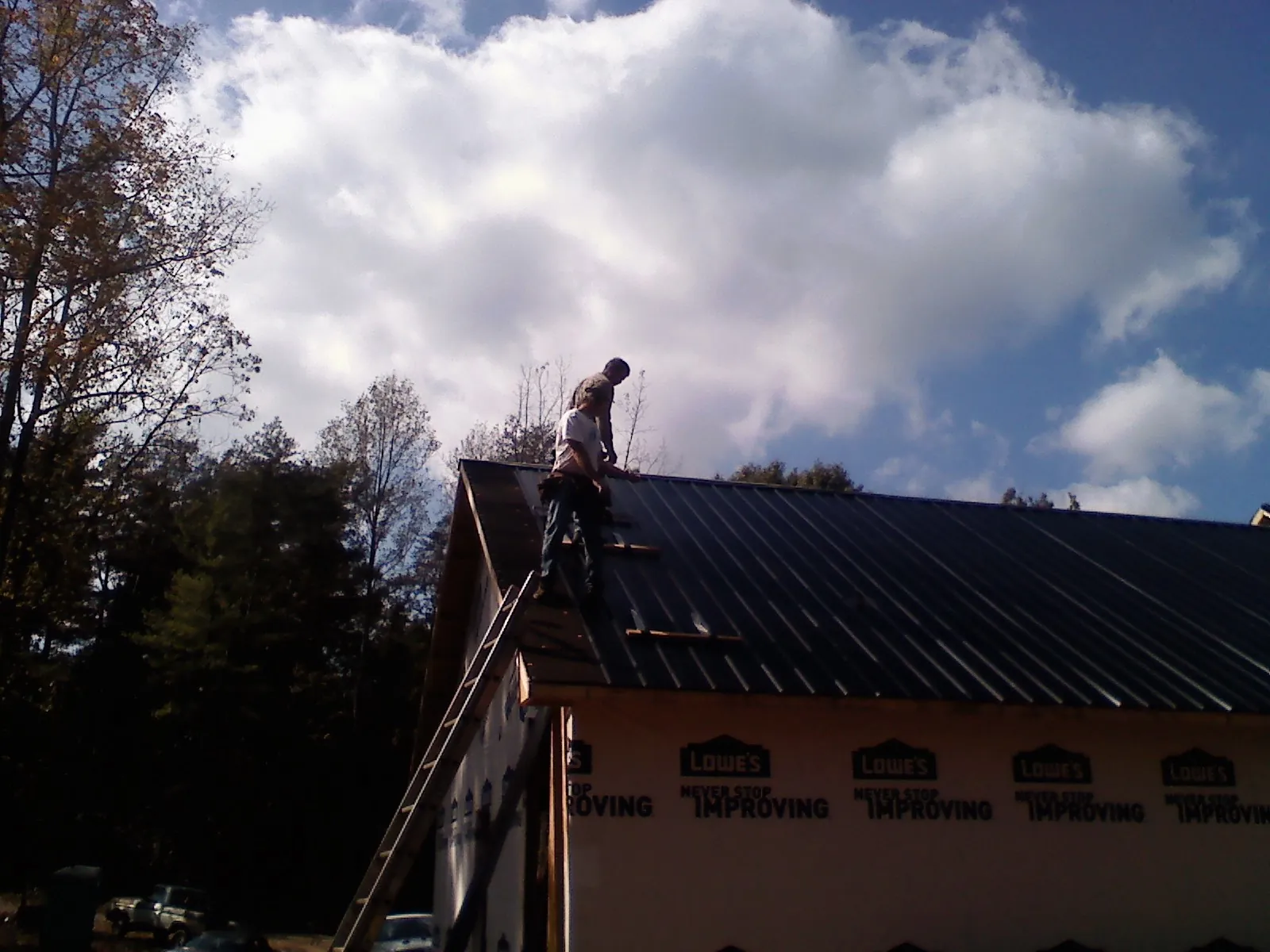 Roofer fastening dark metal panels high against a cloudy sky, from a Roof Inspection job in Williston