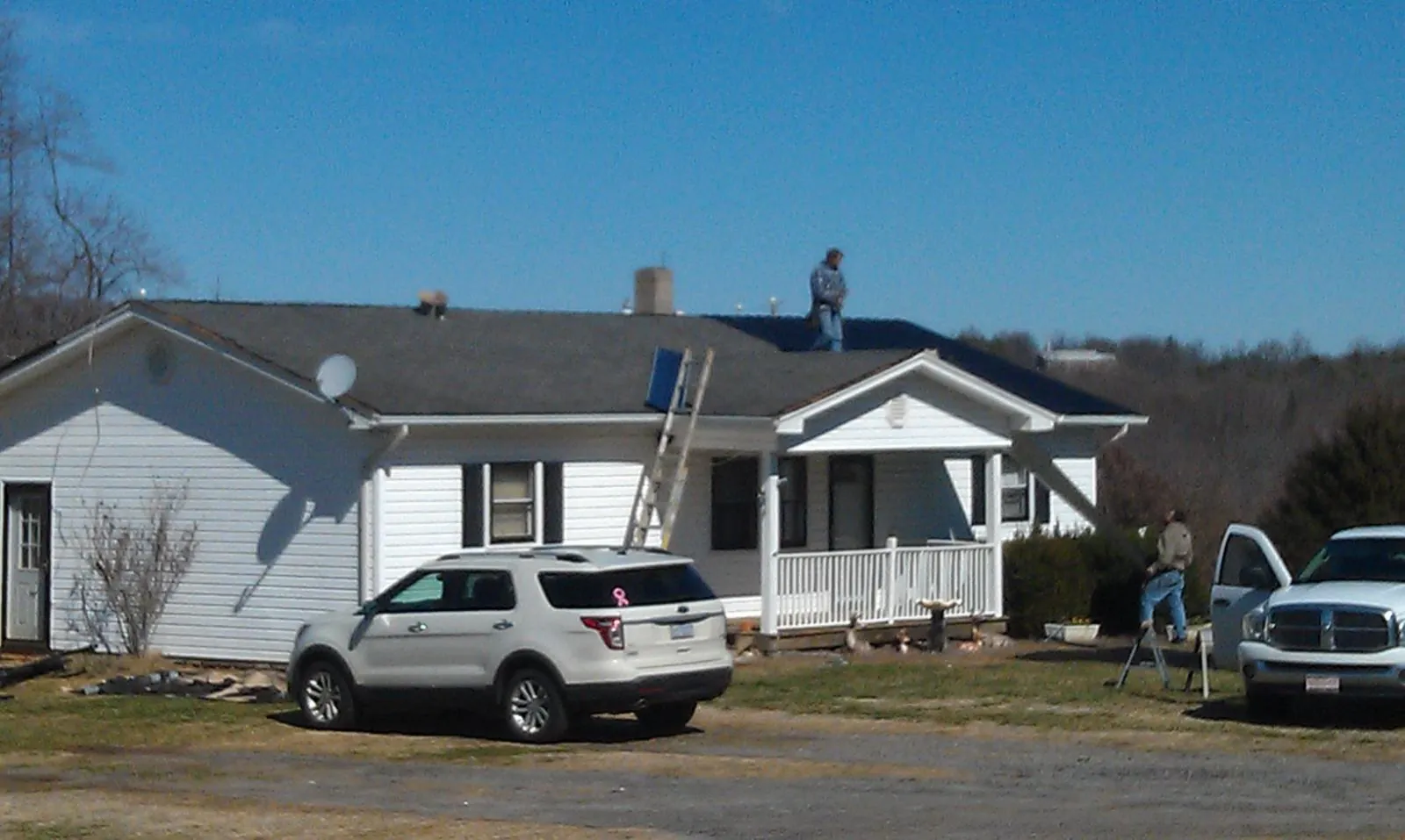 Roofers stripping shingles from a white ranch house roof in Williston