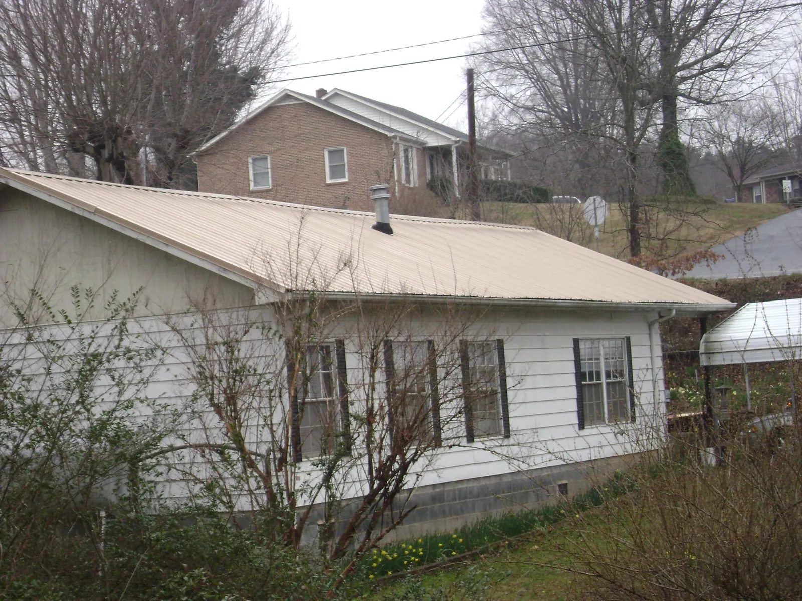 Tan metal roof on a white sided house set into a hillside — Commercial Roofing by Roofing Brothers in Williston